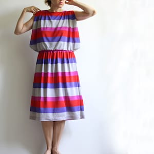 Könnte beinhalten: Ein gestreiftes Midikleid mit geraffter Taille. Das Kleid hat horizontale Streifen in den Farben Grau, Rot, Rosa und Lila.