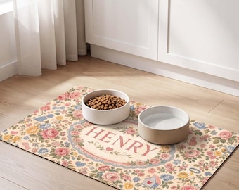 May include: A rectangular pet feeding mat featuring a floral pattern with pink, yellow, and blue roses, small hearts, and bone shapes. The centre displays the name HENRY in red capital letters inside an oval frame, with two white bowls on top.