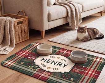 Puede incluir: Una alfombrilla rectangular para mascotas con un patrón de cuadros en rojo, verde y blanco. En el centro, una etiqueta color crema con borde decorativo muestra el nombre HENRY en letras mayúsculas negras, rodeado de ramas de pino y huellas.