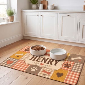 Könnte beinhalten: Eine rechteckige Futtermatte für Haustiere mit einem Patchwork-Design aus orangefarbenen, braunen und cremefarbenen Vichy-Karos. Die Matte zeigt den Namen HENRY in großen braunen Buchstaben, umgeben von braunen Pfotenabdrücken, Knochen und Herzen.