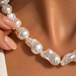 May include: A necklace composed of large, irregular white baroque pearls with a high-luster, iridescent finish. The pearls are strung together in a continuous strand, showcasing their unique, organic shapes and smooth, reflective surfaces.