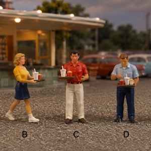 Può includere: Cinque statuette in miniatura etichettate da A a E, ognuna delle quali regge un vassoio di cibo con bevande e snack. La figura A indossa una camicia bianca e pantaloni neri, B un top giallo e una gonna blu, C una camicia rossa e pantaloni bianchi, D una camicia blu e jeans, ed E un top bianco e pantaloni gialli.