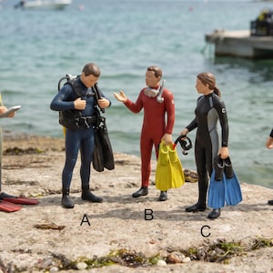 Könnte beinhalten: Fünf Miniatur-Taucherfiguren mit den Bezeichnungen A, B, C, D und E. Figur A trägt einen dunkelblauen Taucheranzug mit Ausrüstung. Figur B trägt einen roten Anzug und hält gelbe Flossen. Figur C trägt einen schwarzen Anzug mit blauen Flossen. Figur D hat einen grauen und gelben Anzug. Figur E trägt einen schwarz-orangen Anzug mit gelben Flossen.