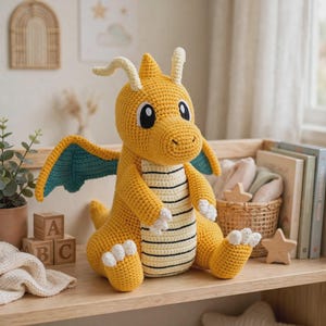 May include: A yellow crochet dragon plush toy with teal wings, white claws, and a cream-colored belly featuring horizontal black stripes. The creature has two antennae on its head and large black and white eyes, sitting in a seated position.