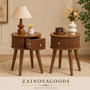 May include: Two round wooden nightstands with fluted sides, three tapered legs, and a single drawer with a small gold knob. One nightstand has an open drawer, while the other is closed. Text at the bottom reads ZAINOVAGOODS ELEVATE YOUR SPACE.