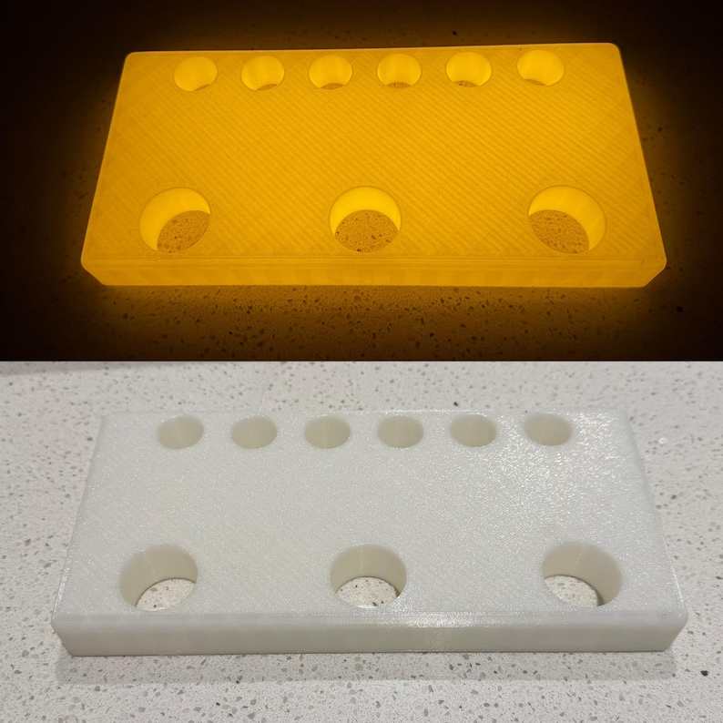 May include: A rectangular white plastic stand featuring six small circular holes along the top edge and three larger circular holes along the bottom edge. The object is shown in two states: one glowing with a bright yellow light and one in white.