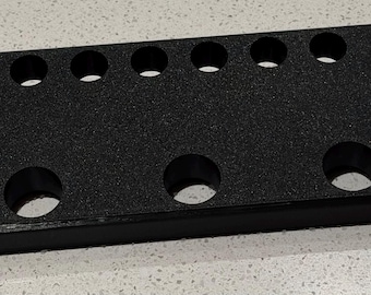 May include: A rectangular black organizer tray with a textured surface featuring six small circular holes arranged in a single row along the top edge and three larger circular holes positioned in a row along the bottom edge of the unit.