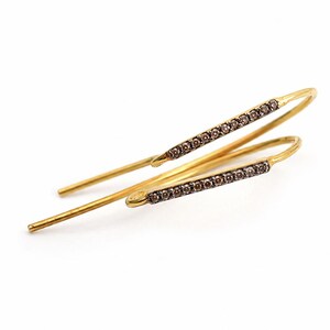 May include: A pair of gold-toned pull-through earrings featuring a slender, curved bar design. Each earring is accented with a row of small, dark-colored stones embedded along the front-facing surface of the metal bar, creating a linear aesthetic.
