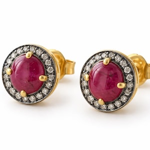 Puede incluir: Un par de pendientes de botón redondos con una piedra preciosa de color rosa intenso en talla cabujón central, rodeada por un halo de pequeños diamantes blancos en un marco de metal oscuro, con garras y cierre de oro amarillo.