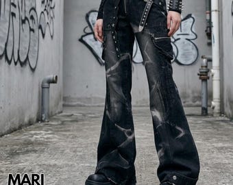 May include: Black denim cargo trousers featuring a faded lightning-like pattern, a front zip fastening, and side cargo pockets. The trousers are styled with a black leather belt with silver-toned hardware and star accents, paired with black platform boots.