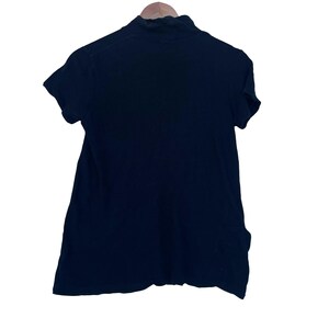 May include: A solid black short-sleeved shirt featuring a mock neck collar. The garment is displayed on a wooden hanger, showcasing a simple, plain design with a straight hemline and a standard fit, constructed from a smooth, opaque fabric.