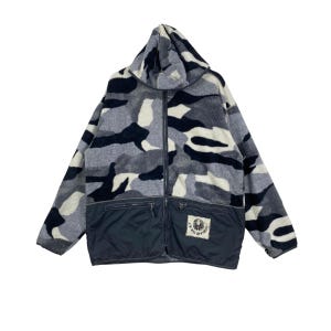 May include: A hooded fleece jacket featuring a gray, black, and white camouflage pattern on the upper portion and a solid black lower section with two zippered pockets. A rectangular patch with the text J.S. NIKI DIVISION is on the lower right.