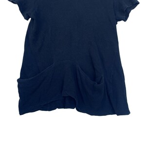 May include: A solid dark navy blue short-sleeved top featuring a round neckline and two large, deep patch pockets positioned at the lower front. The garment has a relaxed, slightly flared silhouette with visible seams and a soft, textured fabric.