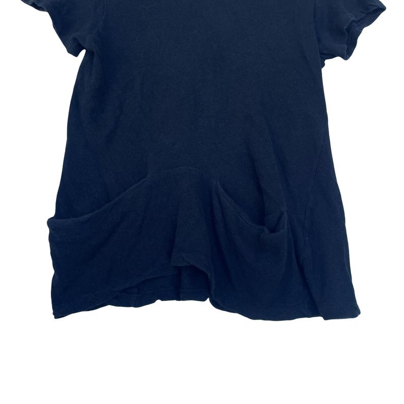 May include: A solid dark navy blue short-sleeved top featuring a round neckline and two large, deep patch pockets positioned at the lower front. The garment has a relaxed, slightly flared silhouette with visible seams and a soft, textured fabric.