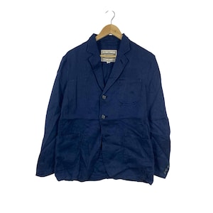 May include: A dark blue blazer with a notched lapel, two front buttons, and three patch pockets. The jacket features a visible interior brand label that reads "HEIRLOOM" and is displayed on a wooden hanger against a plain white background.