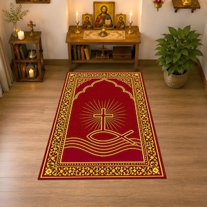 Puede incluir: Una alfombra de oración rectangular con fondo rojo intenso y borde dorado. El centro muestra una cruz dorada sobre un símbolo de pez, con líneas radiantes y líneas horizontales onduladas debajo del diseño del pez.