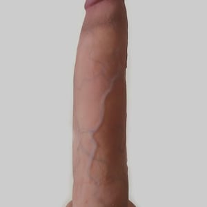 May include: A cylindrical, tan-colored phallic-shaped object with a rounded, slightly darker tip. The surface features a realistic texture with visible raised veins running vertically along the shaft, ending in a flat, circular base at the bottom.