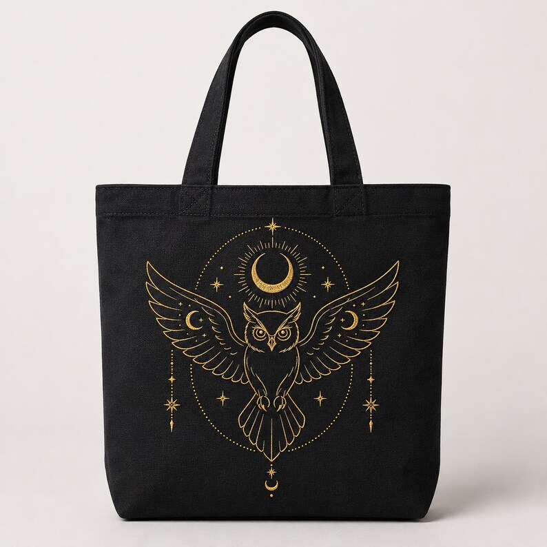 May include: A black tote bag featuring a gold-colored graphic print of an owl with outstretched wings. The design includes a crescent moon, radiating sunburst lines, and various star shapes arranged in a circular pattern around the owl.