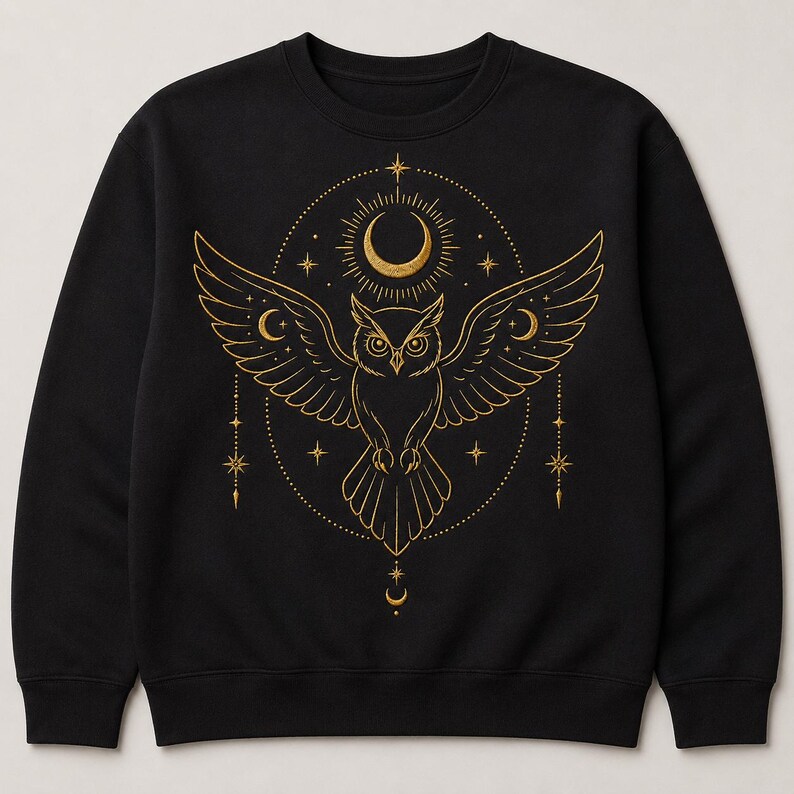 May include: A black long-sleeve sweatshirt featuring a gold-colored graphic print of an owl with outstretched wings. The design includes a crescent moon, stars, and celestial elements arranged in a circular pattern centered on the chest area.