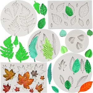 May include: A collection of white silicone molds featuring various leaf and fern shapes, accompanied by several finished leaf castings in vibrant shades of green, orange, and brown. The molds are circular and rectangular, displaying intricate vein details.