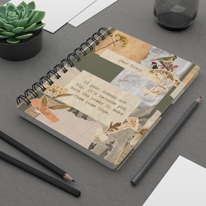 Puede incluir: Un cuaderno de espiral con un diseño de collage en tonos beige, verde oliva y crema. La portada muestra el texto "Dear Diary" y "If your dreams are big, it's because you have the power to make them come true," junto con ilustraciones de flores secas y pájaros.