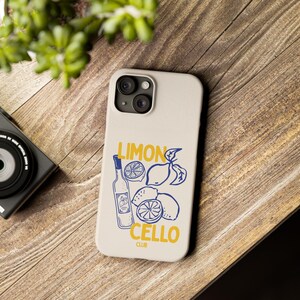 Puede incluir: Una funda de smartphone de color beige claro con una ilustración de líneas azules de una botella y limones, con el texto amarillo LIMON CELLO CLUB impreso en la superficie. El diseño incluye un grupo de limones enteros y cortados junto a la botella.