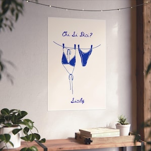Puede incluir: Un póster de pared vertical con un dibujo lineal azul de un bikini colgado en un tendedero con pinzas. El texto Chi Si Dici? está impreso sobre el bikini y la palabra Sicily aparece debajo en una tipografía azul a juego.