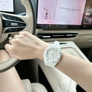 May include: A white wristwatch with an octagonal bezel featuring small, colourful circular markers at each hour position. The watch face has a textured, grid-like pattern with thin, dark hands. The band is a matching white, integrated silicone strap.