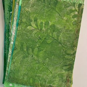 May include: A stack of rectangular paper sheets featuring various shades of green. The top sheet displays a dark green botanical leaf print pattern over a lighter green textured background. Each sheet shows unique ink textures and layered patterns.