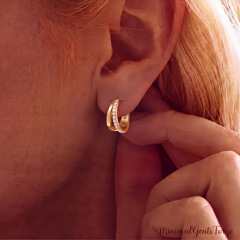 May include: A gold hoop earring featuring a double-band design with one band encrusted with small clear stones. The earring is secured through the earlobe. The text MinimalGentsForge is visible in the bottom right corner of the image.