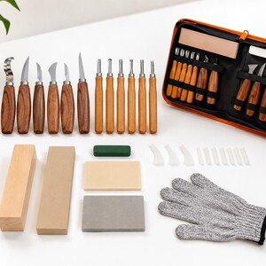 Puede incluir: Un set de tallado en madera que incluye varias hojas de acero con mangos de madera, un estuche de almacenamiento naranja con cremallera, piedras de afilar, bloques de madera, pasta de pulir verde, protectores de dedos y un guante gris resistente a cortes.