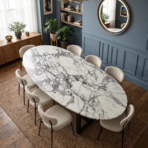 May include: An oval dining table with a white marble top featuring grey veining, supported by a black metal base. Eight chairs with cream-colored textured fabric upholstery and thin black metal legs are arranged around the table.