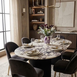 May include: An oval dining table with a white and purple marble top and a black fluted pedestal base, surrounded by six dark grey upholstered chairs with gold-toned legs. A vase with purple and white flowers sits in the centre of the table.