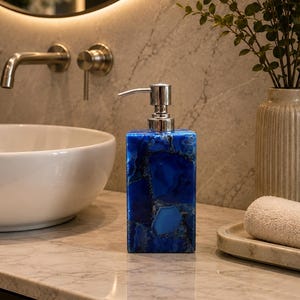 May include: A rectangular soap dispenser crafted from deep blue agate stone with a polished finish. The dispenser features a metallic silver-toned pump mechanism at the top, designed for dispensing liquid soap or lotion in a bathroom setting.
