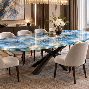 Può includere: Un tavolo da pranzo ovale con un piano in pietra d'agata blu lucidata con venature bianche e dorate, sostenuto da una base a croce in metallo scuro. Otto sedie imbottite in tessuto beige chiaro e gambe in legno scuro circondano il tavolo.
