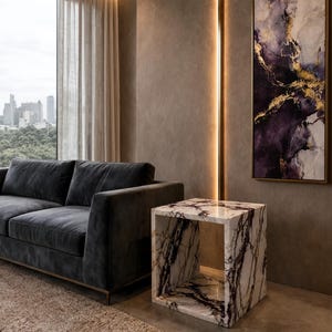 May include: A square side table crafted from white marble with prominent dark purple and black veining. The table features a hollow, open-cube design with polished surfaces, positioned next to a dark gray sofa in a modern interior space.