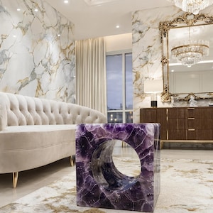 Puede incluir: Una mesa auxiliar cuadrada hecha de piedra amatista de color morado intenso, con un gran recorte circular liso en el centro. La mesa tiene una superficie pulida y reflectante que resalta los patrones cristalinos naturales y las vetas blancas.