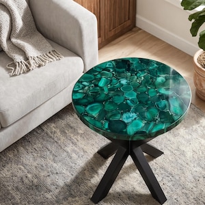 May include: A round side table featuring a tabletop composed of polished green agate slices with varied translucent and opaque textures. The table is supported by a black metal base with four angled legs that meet at a central point.