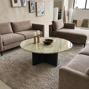 May include: A round coffee table with a polished light green onyx stone top and a black cross-shaped base. On the table are two brass candle holders with white pillar candles and a small dark brown wooden bowl. The table sits on a textured rug.