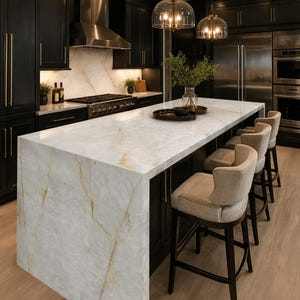 May include: A kitchen island with a white and gold veined stone countertop and waterfall edge, paired with three upholstered bar stools featuring dark wood legs. The kitchen features black cabinetry, stainless steel appliances, and pendant lights.