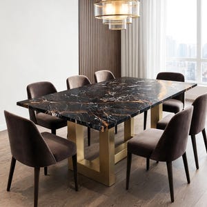 Op de afbeelding: Een rechthoekige eettafel met een zwart marmeren blad met gouden en witte aders, ondersteund door een goudkleurig metalen onderstel. Acht donkerbruine gestoffeerde stoelen met eenvoudige rugleuningen staan rondom de tafel opgesteld.