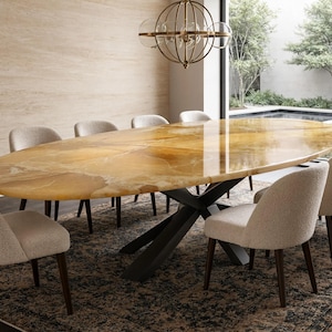 Op de afbeelding: Een ovale eettafel met een gepolijst amberkleurig stenen blad en een donker metalen kruisonderstel, omringd door acht gestoffeerde stoelen met lichtbeige bekleding en donkerhouten poten in een formele eetkamer.