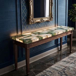 May include: A rectangular console table featuring a polished, backlit green and white agate stone top with a natural crystalline pattern. The table is supported by four dark brown wooden legs with vertical fluting details on the upper sections.