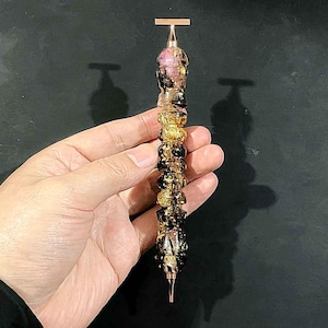 May include: A pen with a rose gold metal clip and tip, featuring a cylindrical body composed of stacked, rounded segments in a marbled blend of translucent pink, deep black, and shimmering gold leaf accents throughout the resin material.