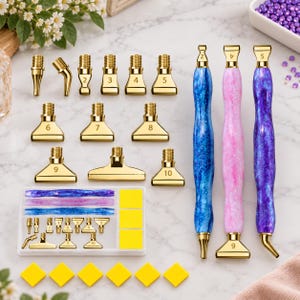Può includere: Un set di strumenti per diamond painting con tre penne in resina con finiture glitterate blu, rosa e viola. Il set include vari puntali in metallo dorato numerati da 2 a 10, un vassoio portaoggetti in plastica bianca e quadrati adesivi gialli.