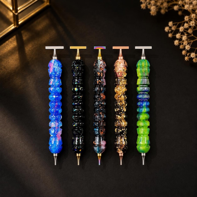 May include: Five diamond painting pens arranged vertically. Each pen features a textured, multi-segmented barrel with distinct color patterns: blue with pink flecks, black with iridescent glitter, dark multi-color, gold leaf, and green with blue swirls.