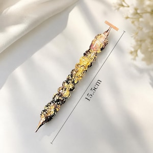May include: A diamond painting drill pen featuring a series of stacked, translucent beads with gold-colored metallic flakes inside. The pen has a rose gold metal tip and a matching top end, with a visible measurement of 15.5cm indicated by a line.