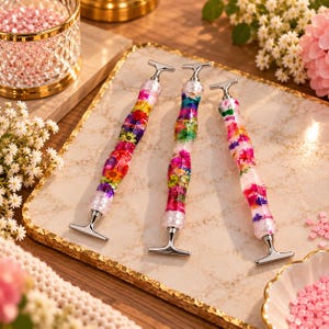 Op de afbeelding: Drie diamond painting pennen met transparante hars handvatten met ingebedde kleurrijke gedroogde bloemen en zilverkleurige metalen T-vormige uiteinden. Elke pen heeft een gestructureerd, golvend gripgedeelte en een metalen punt voor steentjes.