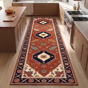 May include: A long rectangular runner rug featuring a deep terracotta red background with a repeating pattern of dark navy blue diamonds, cream-colored geometric borders, and stylized floral motifs in shades of light blue, green, and tan.