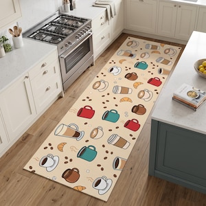 May include: A long rectangular kitchen runner rug featuring a repeating pattern of coffee mugs, to-go cups, coffee beans, and croissants on a light beige background. The mugs are depicted in various colors including red, teal, brown, and white.